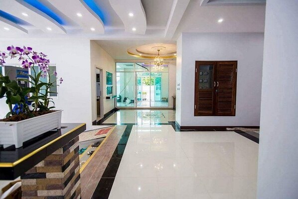 A hotel lobby with a modern design, featuring a central staircase, a reception desk, and a large chandelier.