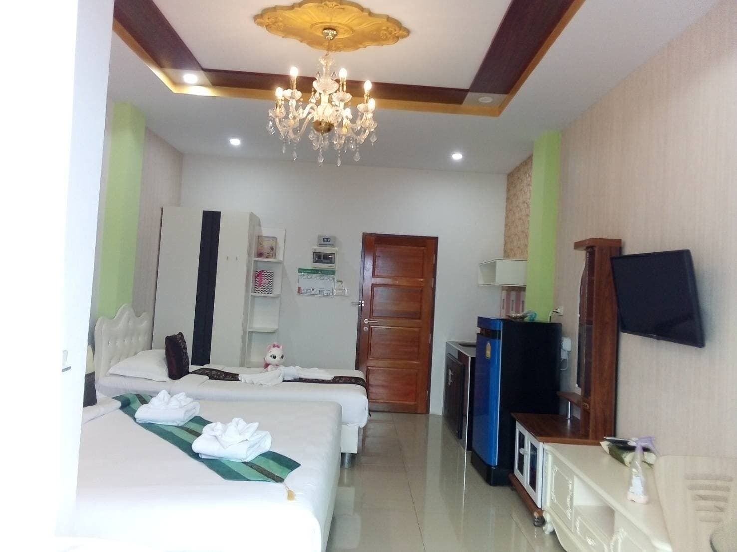 A hotel room with two beds, a television, a minibar, and a chandelier.