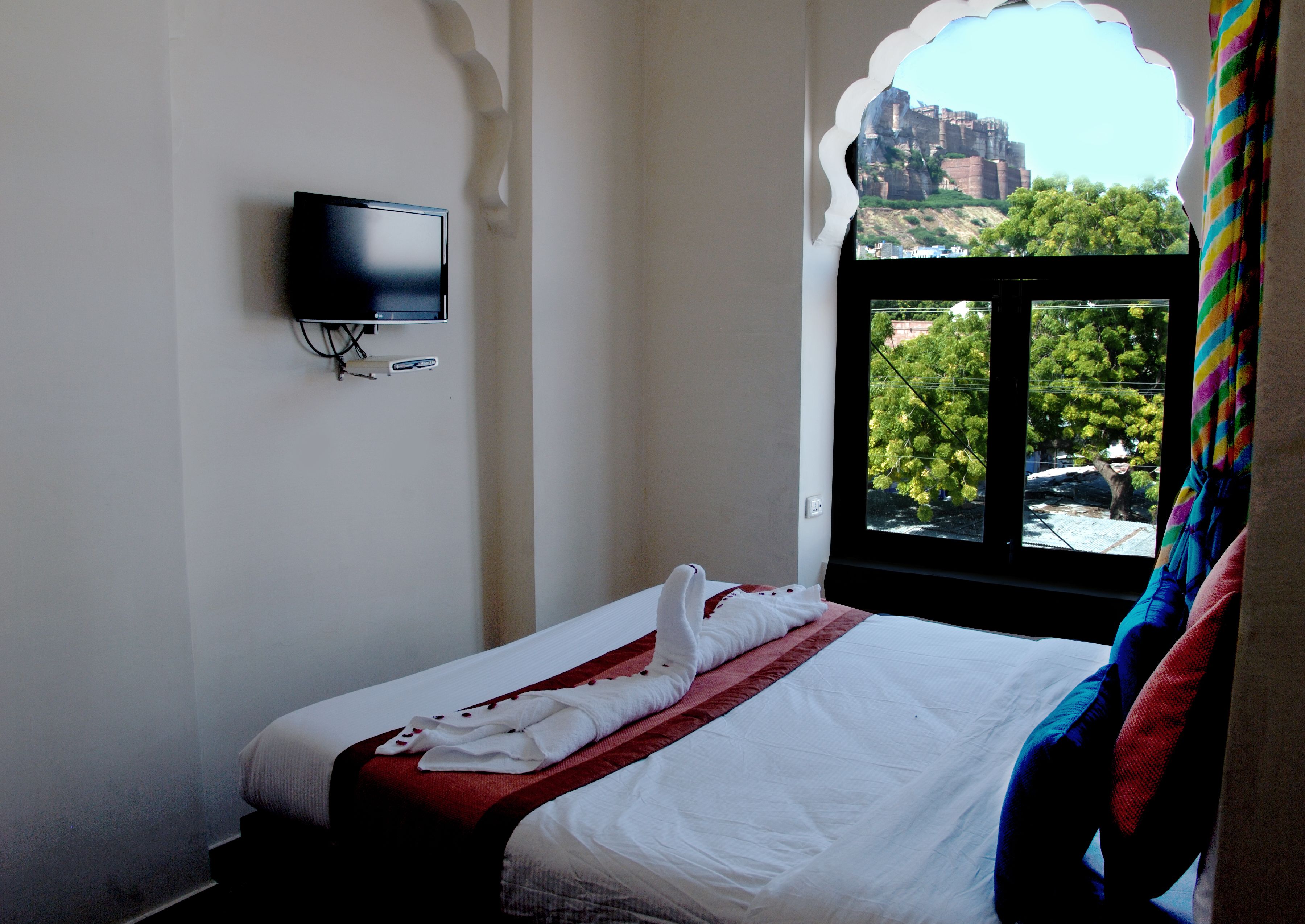 A hotel room with a bed, a television mounted on the wall, and a window with a view of trees and a building.