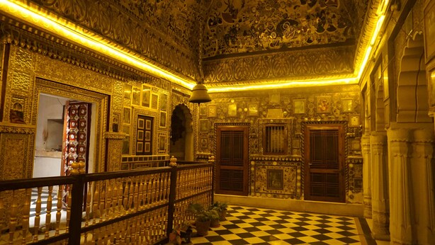 An ornate room with intricate wall and ceiling designs, a checkered floor, and a wooden railing. - Nirvana Home (Jodhpur)