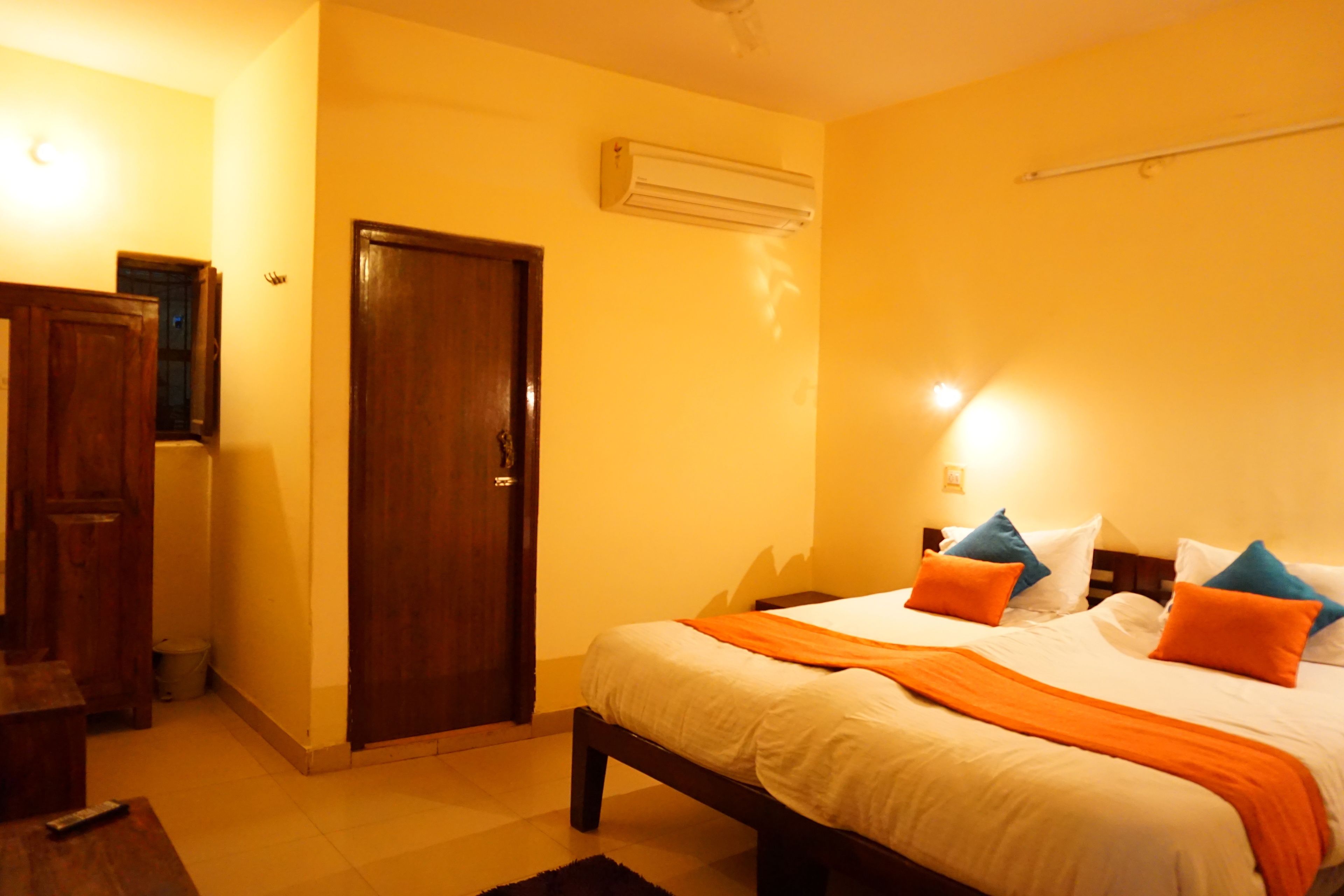 A hotel room with a bed, wooden wardrobe, and an air conditioning unit.