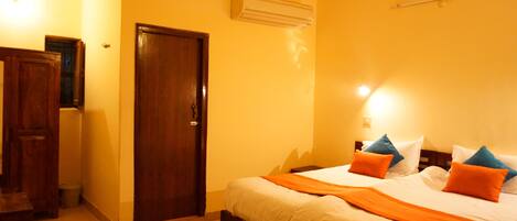 A hotel room with a bed, wooden wardrobe, and an air conditioning unit.