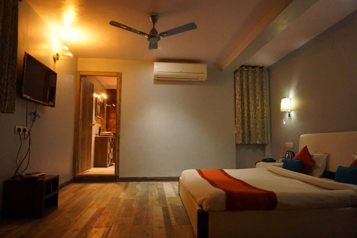 A hotel room with a bed, a ceiling fan, an air conditioning unit, a television, and a doorway leading to a bathroom.