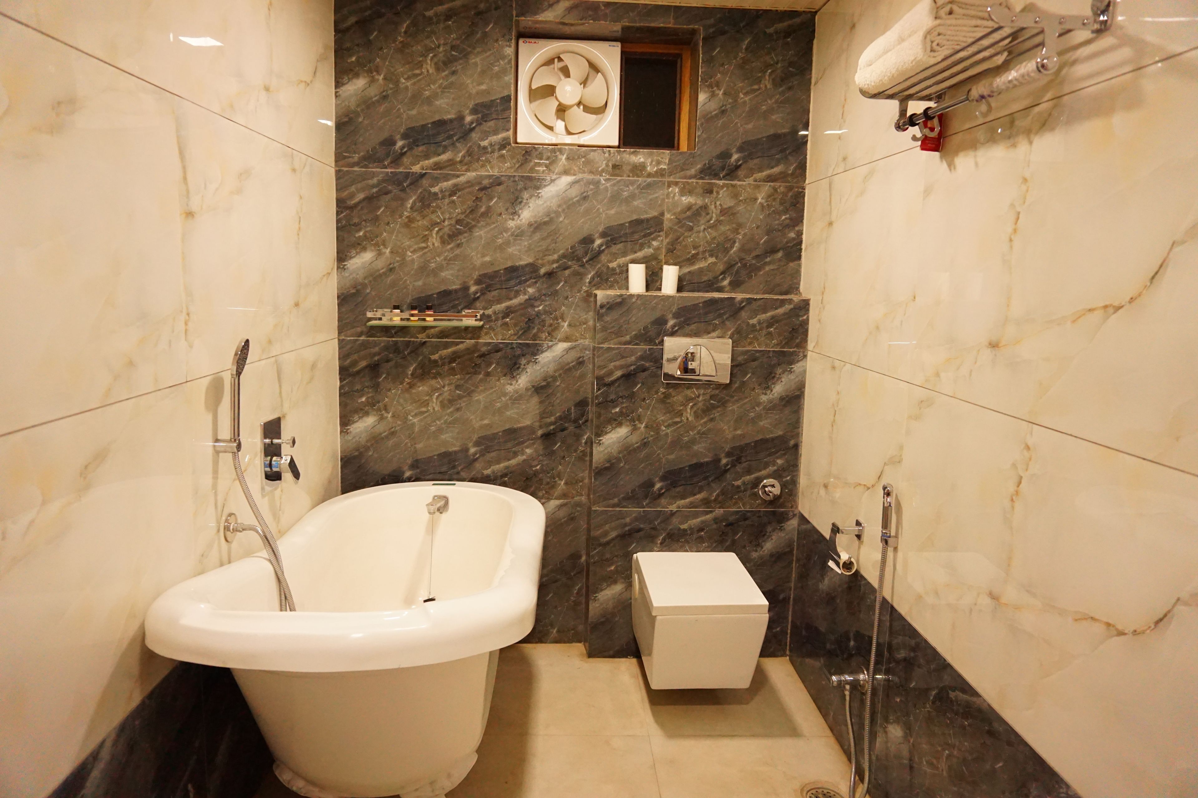 A bathroom with a freestanding bathtub, a towel rack, a small shelf with toiletries, and a marble wall.