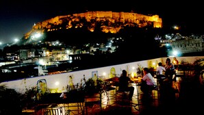 A rooftop restaurant with outdoor seating overlooking a historic fort. - Nirvana Home (Jodhpur)