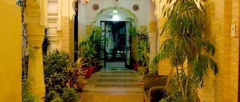 A corridor with potted plants, a ceiling fan, and a traditional archway leading to a room.