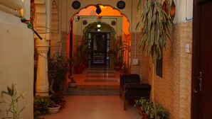 A corridor with a tiled floor, potted plants, a hanging plant, and a door at the end. - Nirvana Home (Jodhpur)