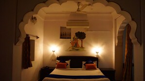 A bedroom with a bed, two nightstands, a ceiling fan, an air conditioning unit, and a wall-mounted artwork. - Nirvana Home (Jodhpur)