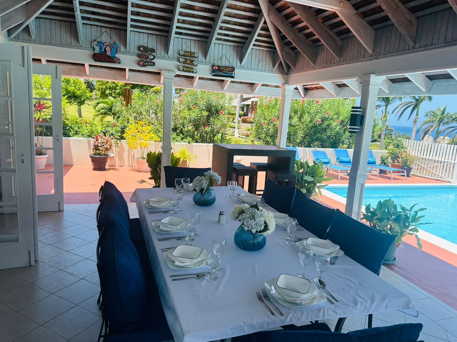A covered outdoor dining area with a table set for four, surrounded by chairs and a view of the pool.