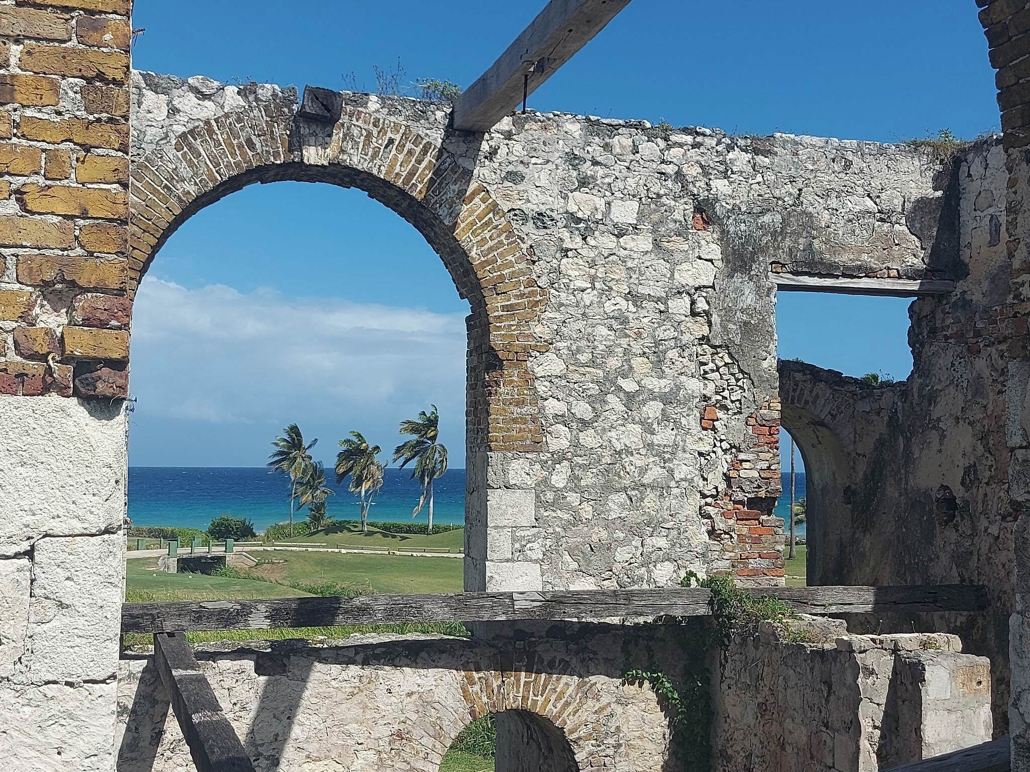 A stone archway leading to a view of the ocean and palm trees.