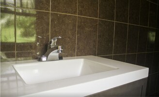 A bathroom with a white sink, chrome faucet, and dark brown tiled walls.