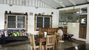 Una habitación con una mesa de comedor de madera, sillas, un sofá con bolsos y un ventanal grande.