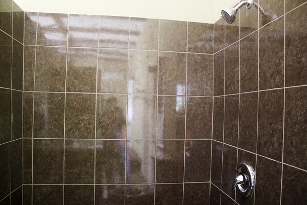 Zona de ducha con azulejos, cabezal de ducha de mano y grifo empotrado en la pared.