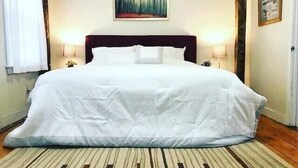 Un grand lit avec du linge de lit blanc, deux lampes de chevet, un tableau au-dessus du lit et un tapis à rayures sur le sol.