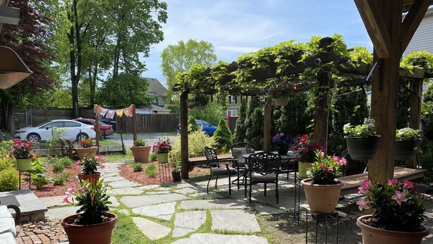 Une terrasse de jardin avec un sol en pierre, des plantes en pot et du mobilier d’extérieur.