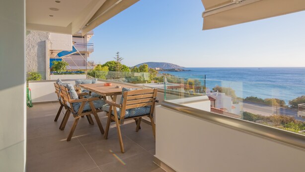 A balcony with a wooden table and chairs, a glass railing, and a view of the sea. - Best Seaview Attica Apartment “Sikinos” (Saronida, Athens)