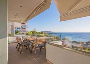 A balcony with a wooden table and chairs, a glass railing, and a view of the sea. - Best Seaview Attica Apartment “Sikinos” (Saronida, Athens)