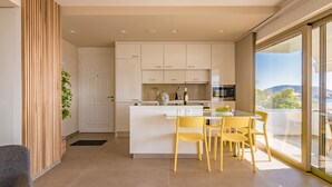 A modern kitchen with white cabinets, a central island with chairs, and a view through large sliding glass doors. - Best Seaview Attica Apartment “Sikinos” (Saronida, Athens)