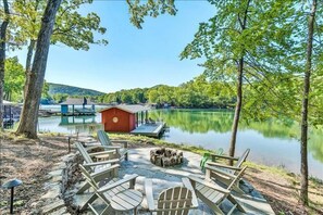 A lakeside deck with Adirondack chairs, a fire pit, and a small red building. - 3 Bedrooms, 1 Flex Room, 3 Bathrooms!  Hot Tub, Wifi & Pet Friendly!  Great Getaway For Any Season! (Huddleston)