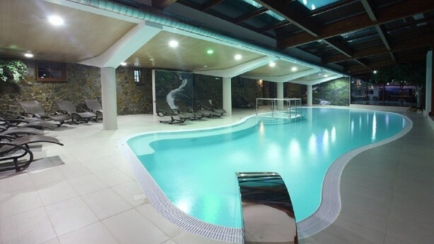 Una piscina interior de diseño curvo, rodeada de sillones de descanso y un muro de piedra con un mural.