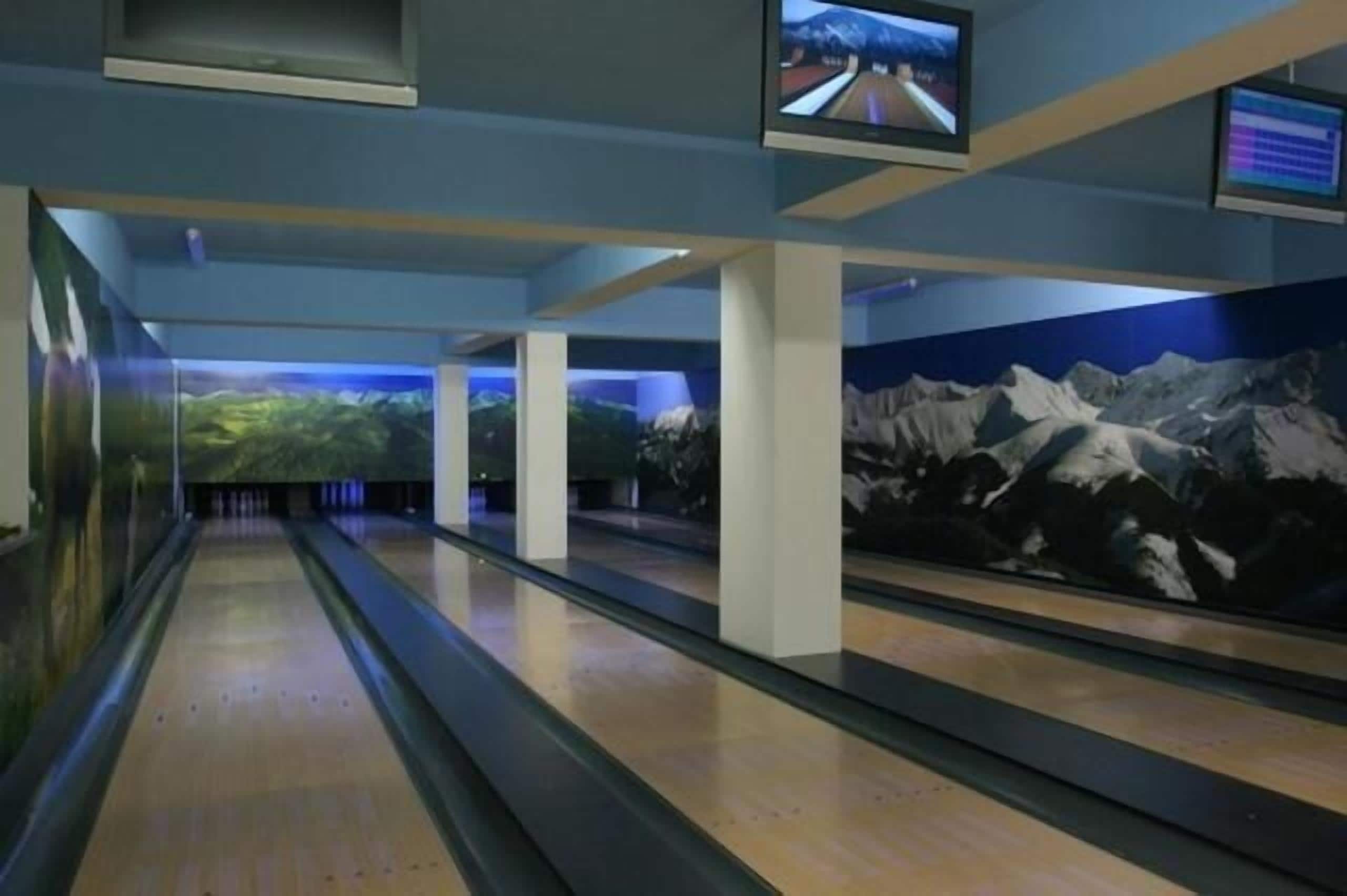 En bowlinghal med flere baner, overvågningsskærme i loftet og et vægmaleri af bjerge.