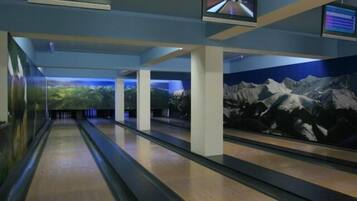 En bowlinghal med flere baner, overvågningsskærme i loftet og et vægmaleri af bjerge.