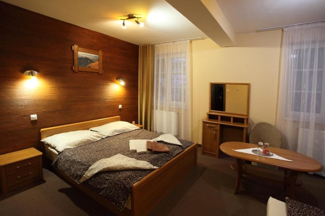 A hotel room with a wooden bed, bedside tables, a desk, a chair, and a large window with curtains.