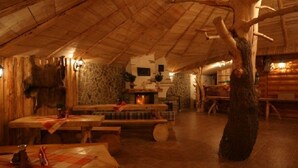 Un interior rústico con paredes de madera, una chimenea de piedra y un tronco de árbol grande como elemento central.