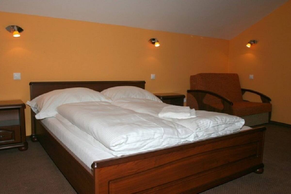 Una cama bien tendida en una habitación con dos mesitas de noche y una silla.
