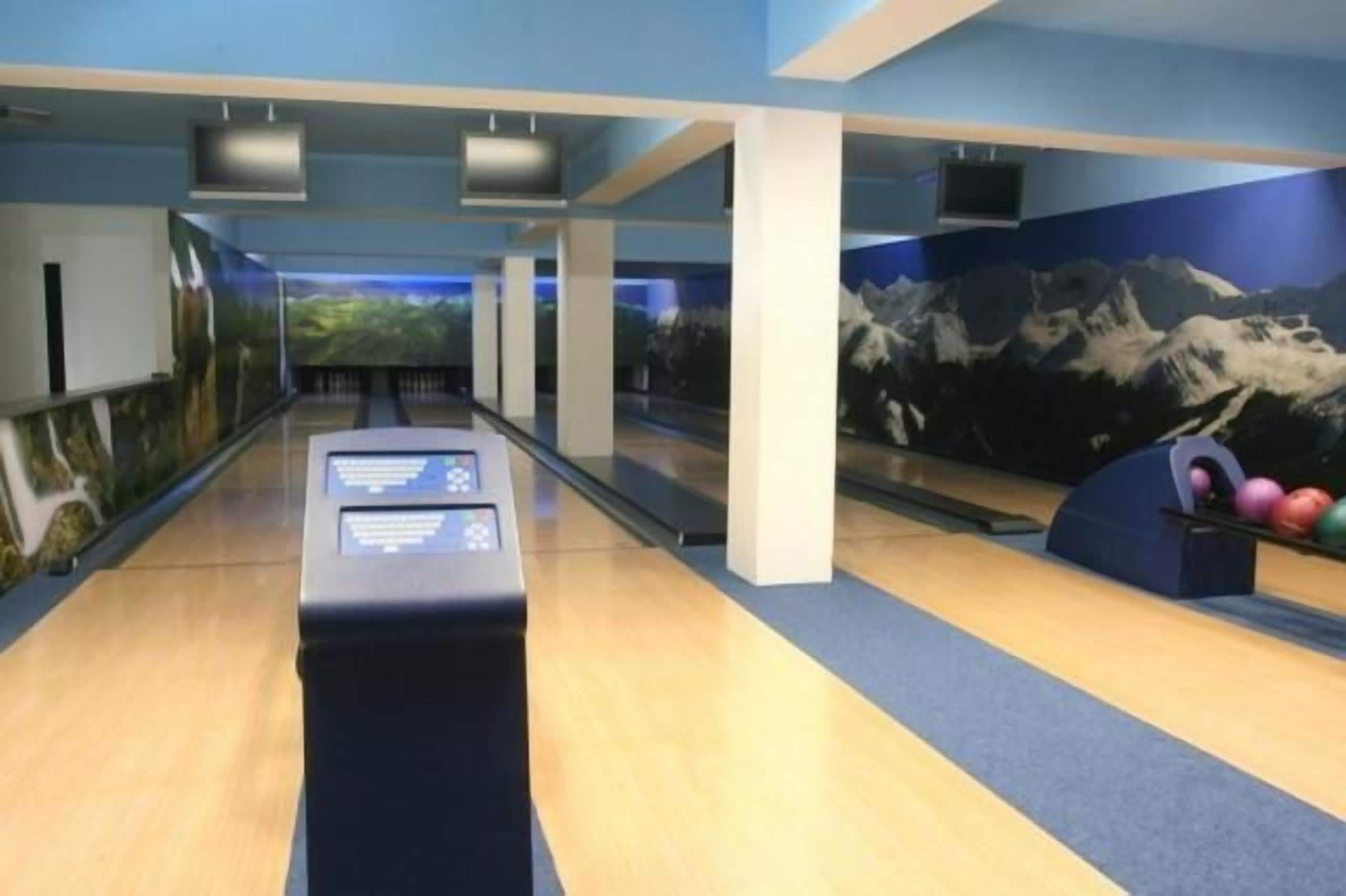 A bowling alley with a wooden floor, a bowling ball return, and a wall mural of mountains.