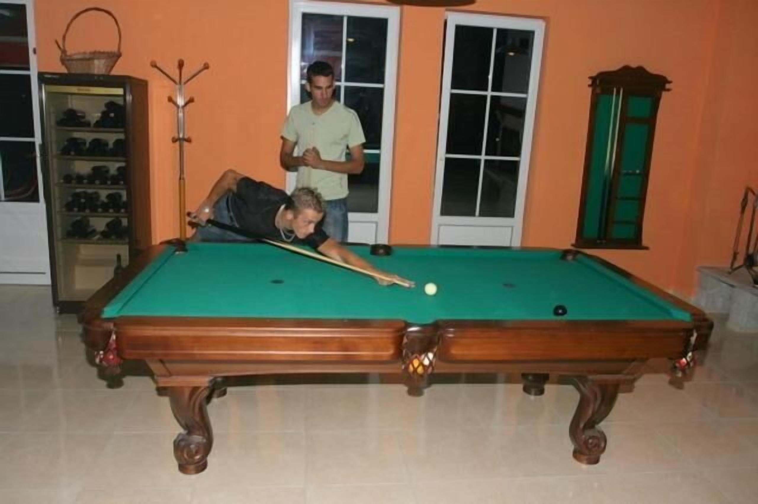 A pool table in a room with a tiled floor, a shoe rack, and a window with a view.