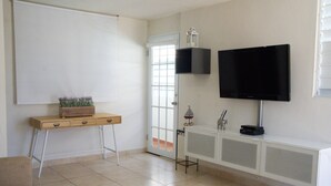 Une pièce comprenant un tableau blanc, un téléviseur fixé au mur, une petite table avec une plante et un meuble avec des tiroirs.