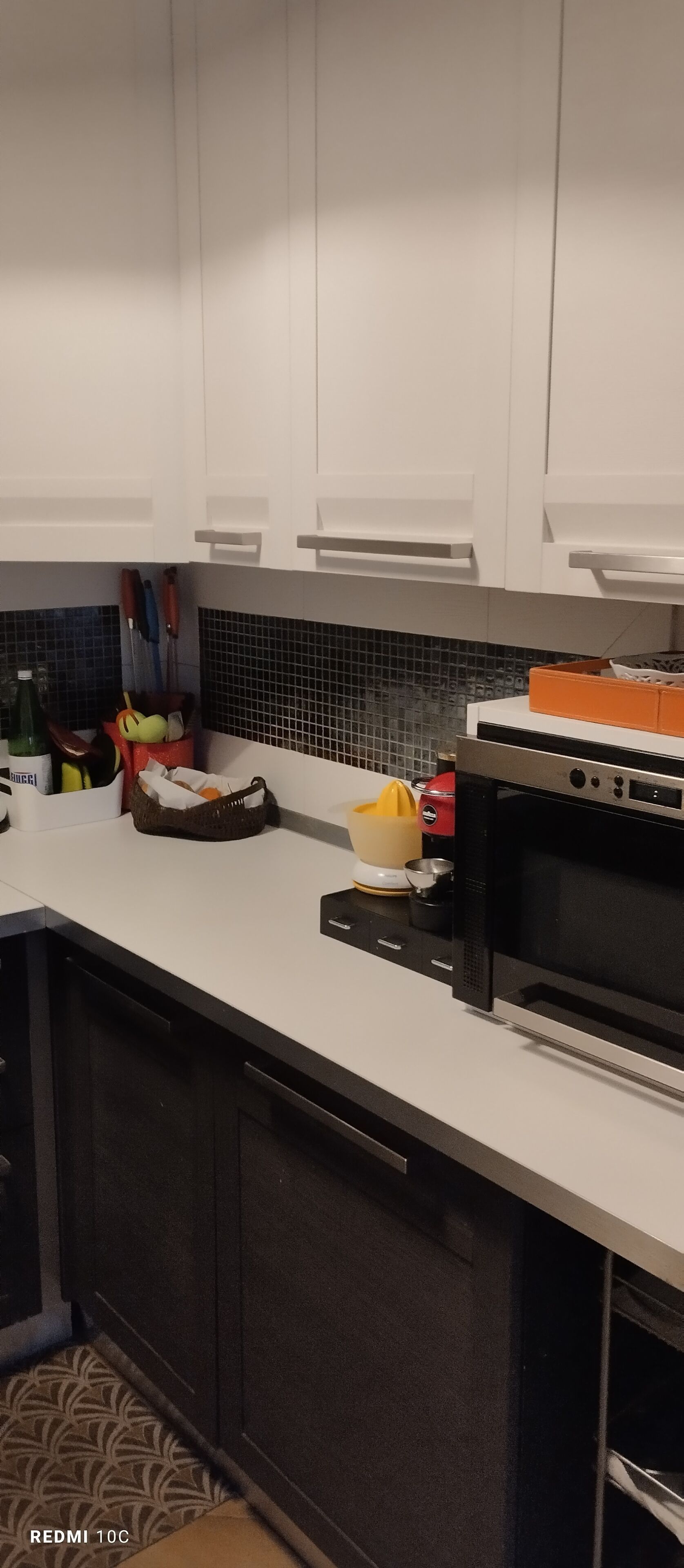 Una cocina con armarios blancos, una encimera negra y un horno de acero inoxidable. Se observan diversos utensilios y electrodomésticos.