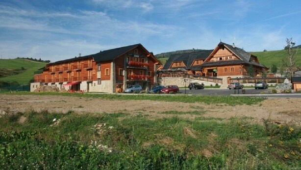 Ein großes Holzgebäude mit mehreren Balkonen, einer gepflasterten Auffahrt und geparkten Autos.