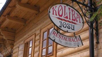 Un edificio de madera con un letrero que dice "KOLIBA RESTAURACIA" y horario de atención "08:00 - 22:00".