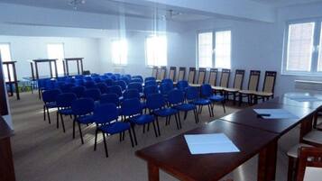 Une salle de conférence avec des rangées de chaises bleues, une longue table et de grandes fenêtres.