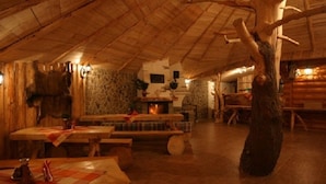 A rustic interior with wooden walls, a stone fireplace, and a large tree trunk centerpiece. - Chaty Josu Zuberec (Zuberec)