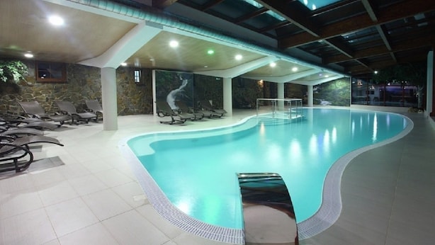 An indoor swimming pool with a curved design, surrounded by lounge chairs and a stone wall with a mural. - Chaty Josu Zuberec (Zuberec)