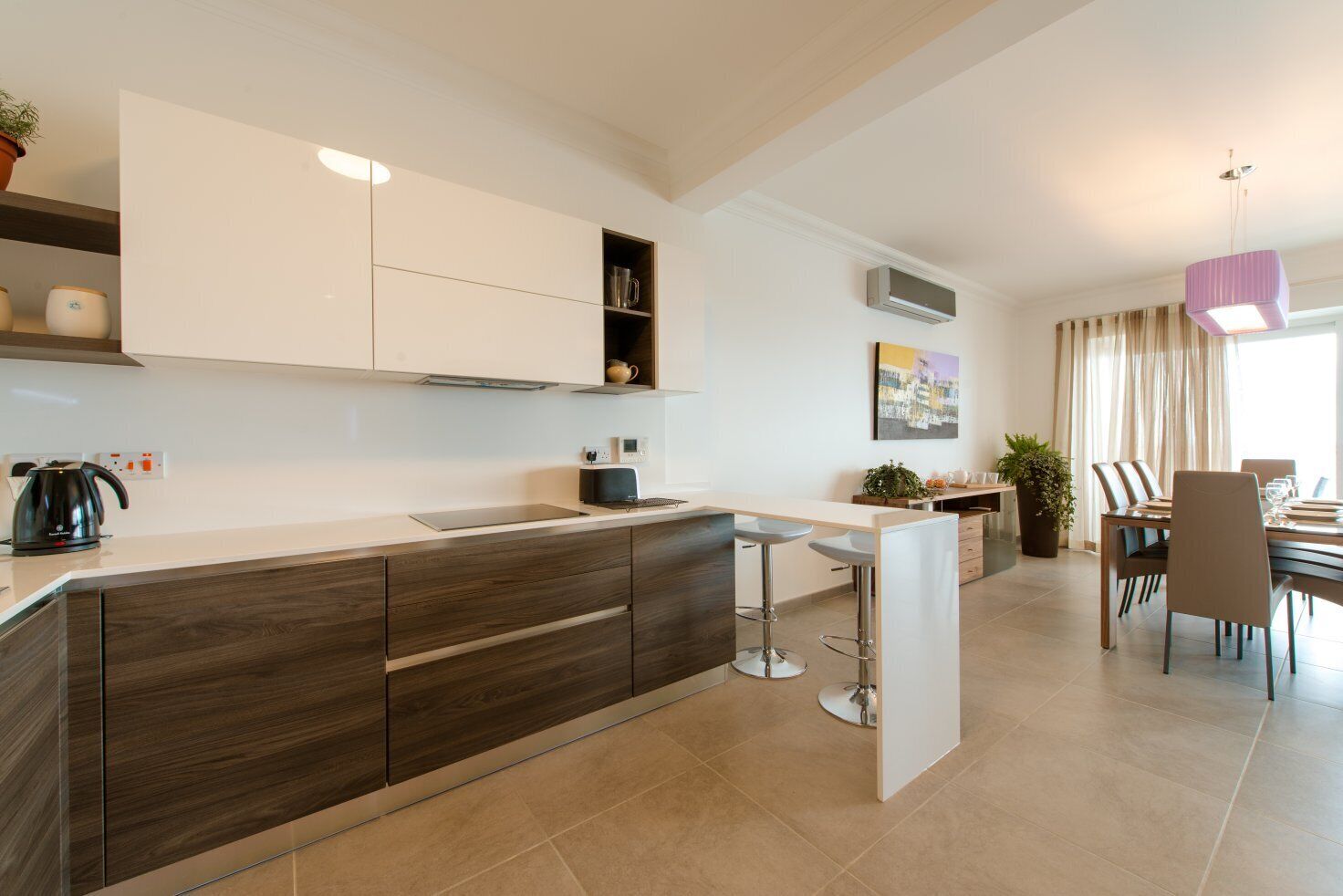 Een moderne keuken met een centraal eiland, barstoelen en een eethoek met een tafel en stoelen.