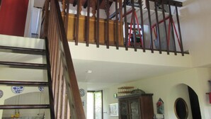 Una escalera con barandilla de madera que conduce a un área del segundo piso, con un ventilador de techo y una silla roja.