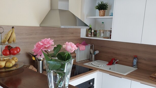 Una cocina con gabinetes blancos, una campana extractora de acero inoxidable, un lavamanos y una encimera con un jarrón de flores.