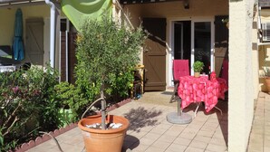 Un patio con suelo de baldosas, una mesa con mantel rojo y una planta en maceta.