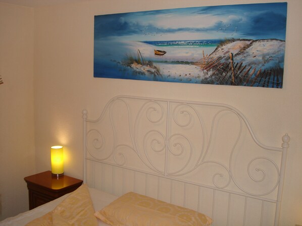 Een slaapkamer met een bed, een nachtkastje met een lamp, en een schilderij van een strand.