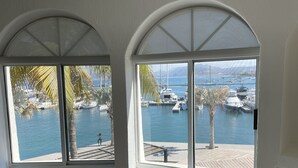 Una habitació amb grans finestres d'arc gòtic que donen a un port esportiu ple de vaixells i palmeres.