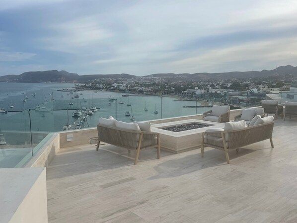 Terraza con mobiliario de mimbre y una chimenea, con vistas a un puerto deportivo lleno de barcos.