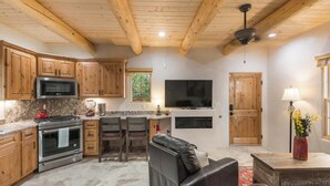 A kitchen with wooden cabinets, a microwave, and a stove. There is a dining area with chairs and a table. A television is mounted on the wall. - Clean and Comfortable, Walk to The Plaza, Ft Marcy (Santa Fe)