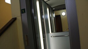 An elevator interior with a metallic door, a handrail, and a wall-mounted sign indicating the floor level.