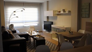 A modern living room with a sofa, TV, dining table, and chairs.