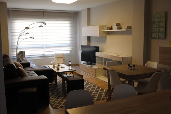 Una sala moderna con sofá, televisor, mesa de comedor y sillas.