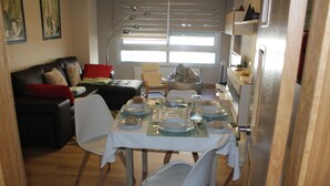 A dining area with a table set for four, surrounded by white chairs. A sofa and a bean bag chair are visible in the background.